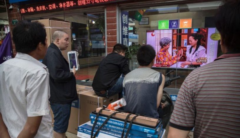 گروهی از چینی‌ها یک برنامه تلویزیونی را در ویترین یک فروشگاه لوازم الکترونیکی در شهر ووهان در استان هوبی، چین تماشا می‌کنند. (Kevin Frayer/Getty Images)