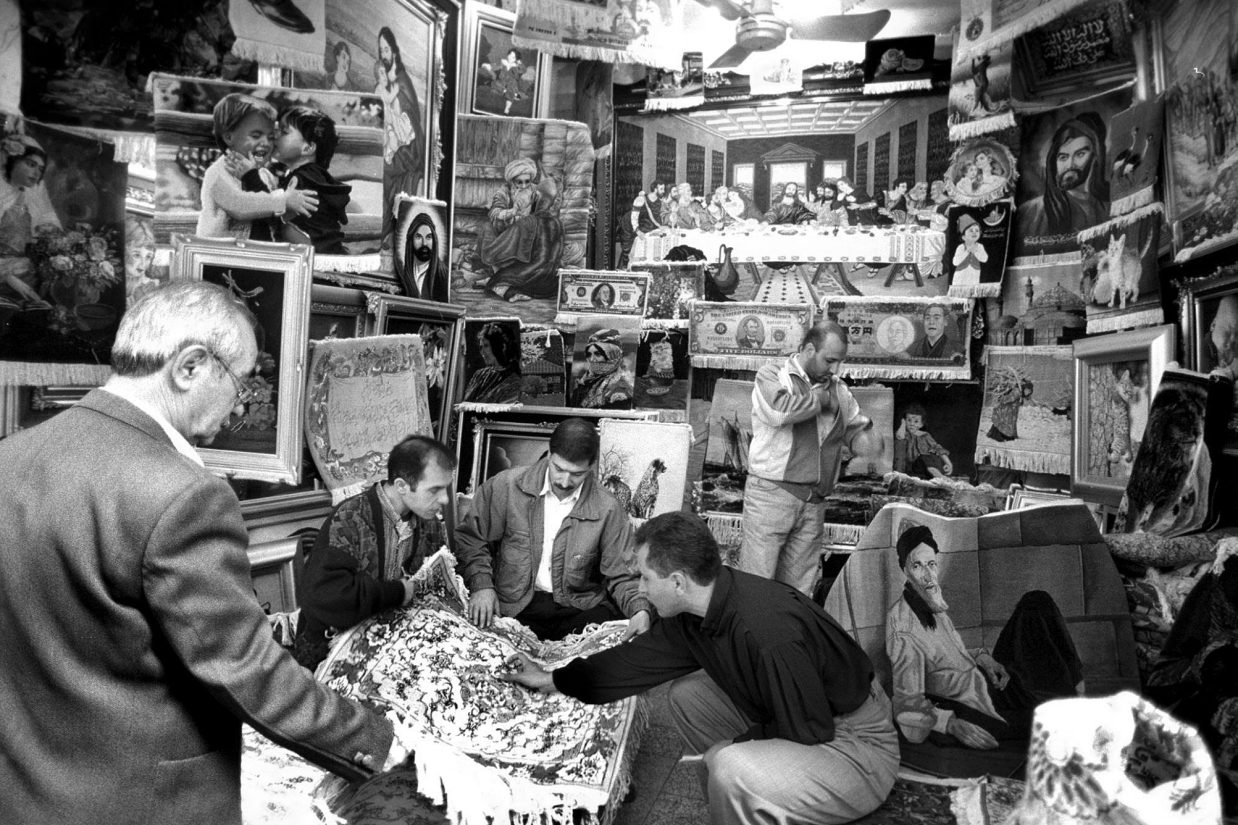 TEHRAN, IRAN:  A picture dated 08 November 1998 shows Iranians inspecting a carpet in an Aladin's cave of pictorial rugs depicting a range of subjects from the Last Supper to dollar bills (background), in Tehran bazaar. Iran's carpet industry is in crisis, grim news for government already grappling with a plunge in world crude oil prices and its national currency while unemployment and the national debt soars. Carpet exports, the top foreign currency earner after oil, have sunk from 1.8 billion dollars in 1994 to around one billion dollars in the last fiscal year ended March, and earning after forecast to drop further to no more than 700  million to 800 million this year. (Photo credit should read ATTA KENARE/AFP/Getty Images)
